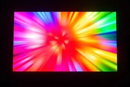 A vibrant, high-definition TV screen displaying a dynamic burst of rich, saturated colors — deep crimson, electric blue, luminous gold, and emerald green — radiating outward in smooth gradients and soft glows, as if the screen is glowing from within. The surrounding environment is dark and minimalistic, emphasizing the screen’s luminosity. No text, logos, or UI elements visible on the screen. The image conveys energy, clarity, and visual brilliance, capturing the essence of a TV screen 'shining