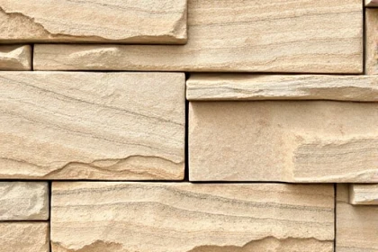 A close-up view of natural stone panels used for cladding a building facade, showcasing the texture, color variations, and subtle shadows that highlight the stone's depth and craftsmanship, with a neutral background that emphasizes the stone's surface details