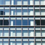 A modern building facade featuring sleek thermopane windows arranged in a grid pattern, showing clear glass panels with metallic frames, reflecting sunlight, with a clean architectural design and minimalist aesthetic, smallHQ