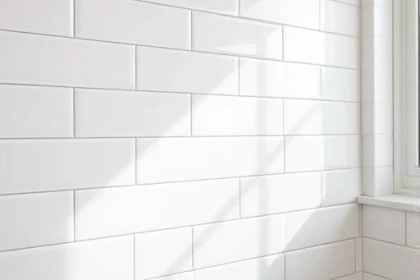 A close-up view of a modern bathroom wall covered in elegant white ceramic tiles with subtle gray grout, arranged in a uniform grid pattern. Soft natural light from a nearby window highlights the clean, minimalist aesthetic, creating a serene and inviting atmosphere.