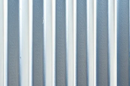 A close-up of a galvanized steel sheet used for a fence, showing its textured zinc coating with a subtle crystalline pattern, placed vertically as part of a modern outdoor fence under natural daylight, with soft shadows and no background distractions