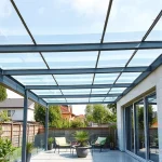 A modern terrace with a transparent polycarbonate roof, supported by sleek metal beams, allowing natural light to filter through; the terrace features minimalist outdoor furniture, potted plants, and a view of a green garden or suburban backyard under a clear sky; high detail, realistic textures, soft daylight lighting, no people visible